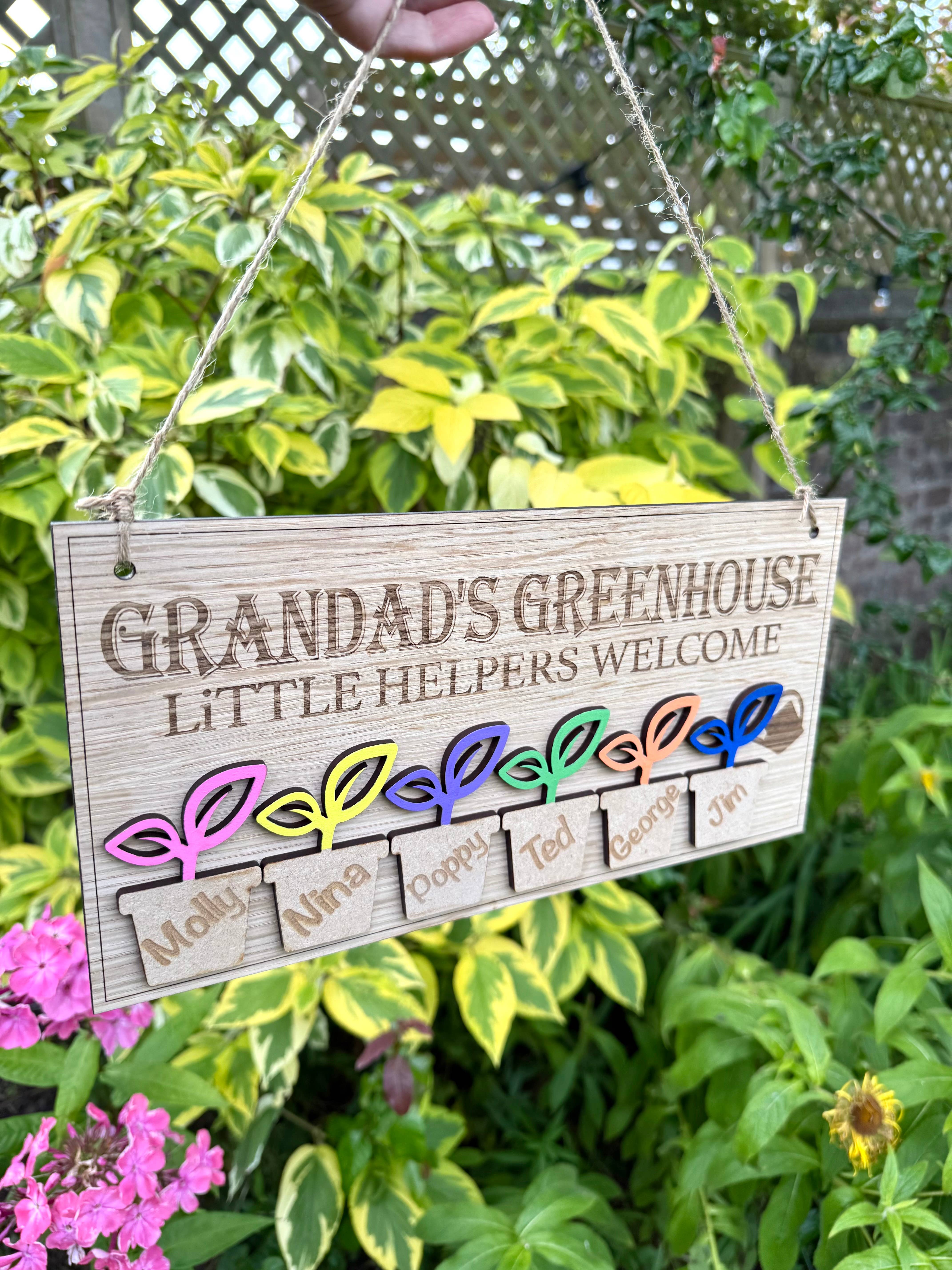 Personalised Grandadโs Greenhouse wooden sign with little helpers welcome text and 6 plant pots with childrens names hanging in a garden